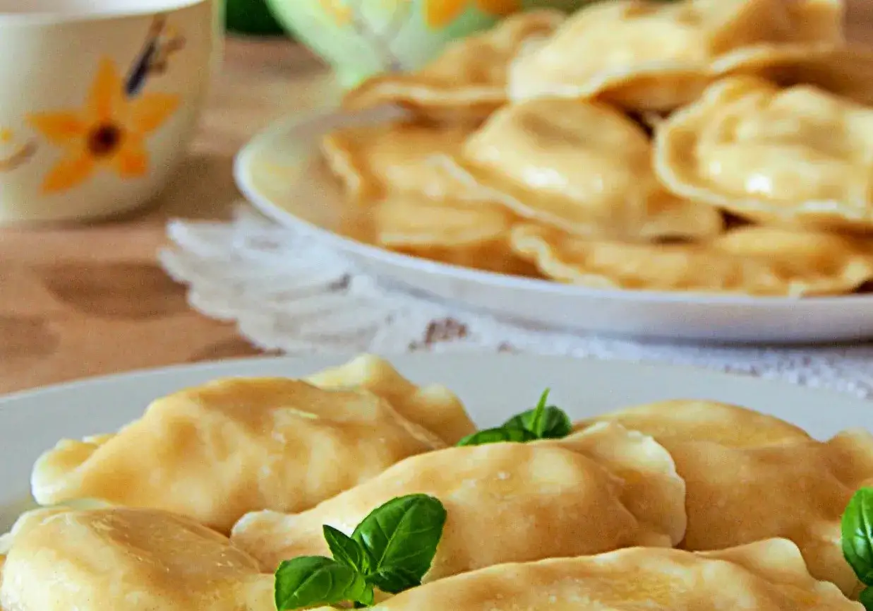 Słowackie pierogi z bryndzą na talerzu, ozdobione listkami bazylii.