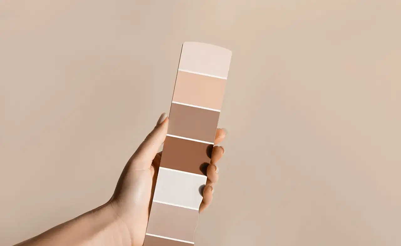 Dłoń trzyma paletę kolorów, od jasnych beżów po ciemne brązy. Zastanawiasz się, czy można pomalować tapetę?