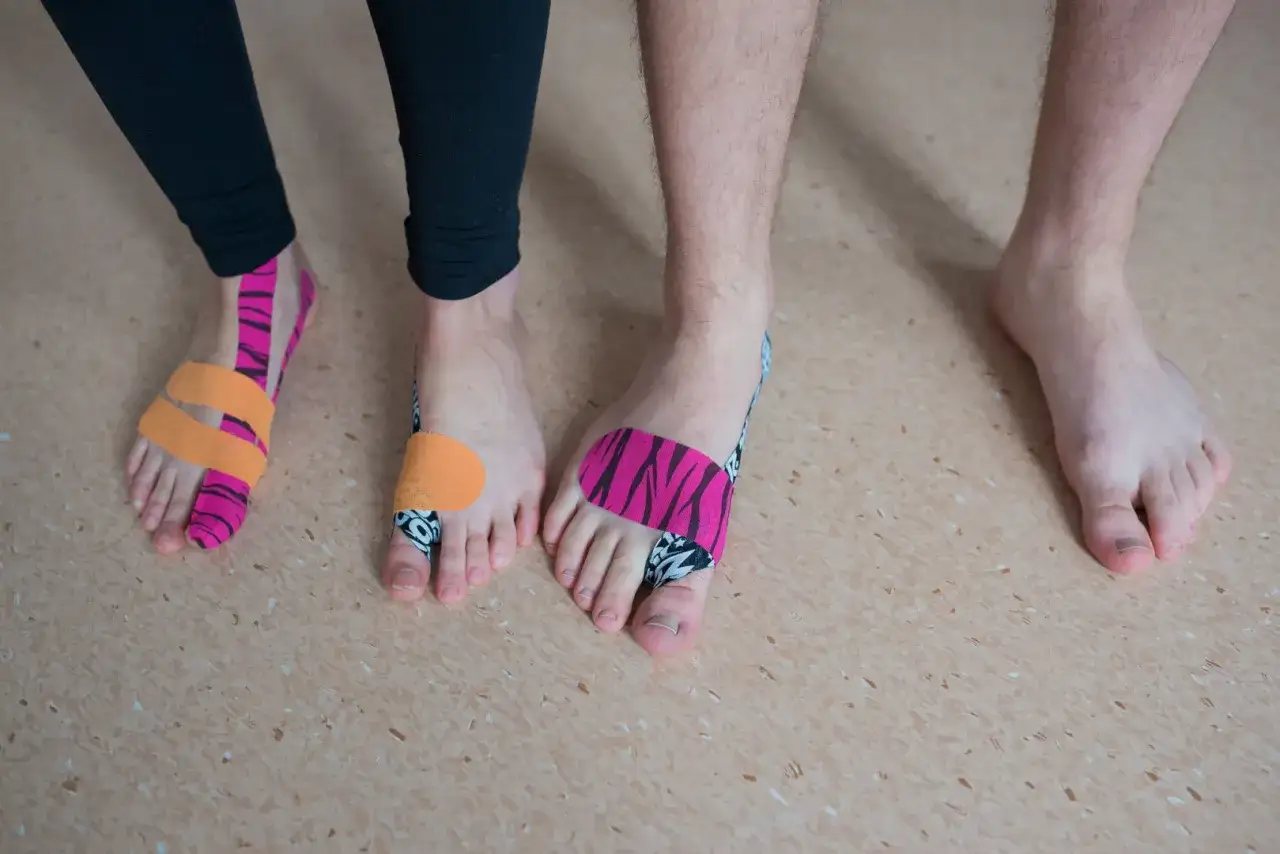 Kolorowe plastry na stopach, co pomaga na ból haluksa. Dwie osoby z kinezjotapingiem na palcach.
