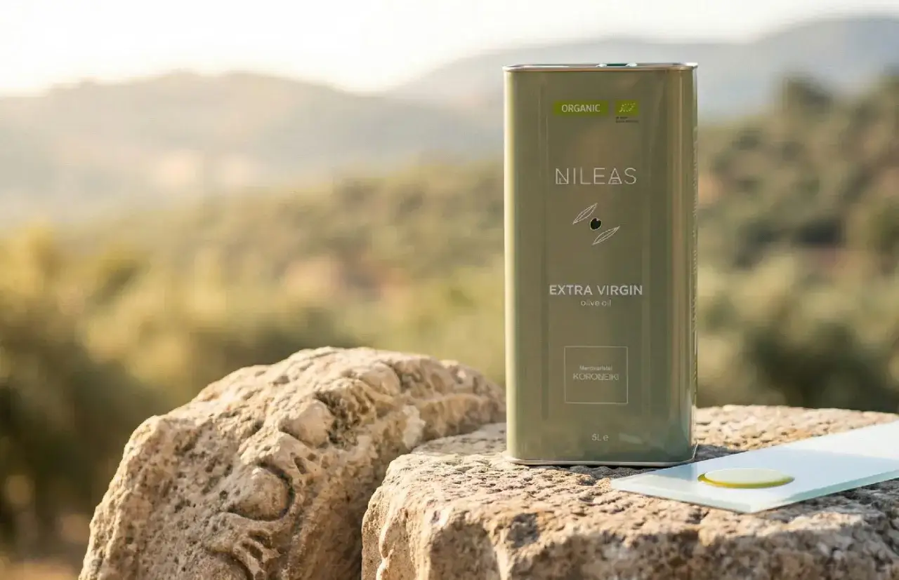 Metalowa puszka oliwy z oliwek NILEAS Extra Virgin na kamieniu, w tle krajobraz.