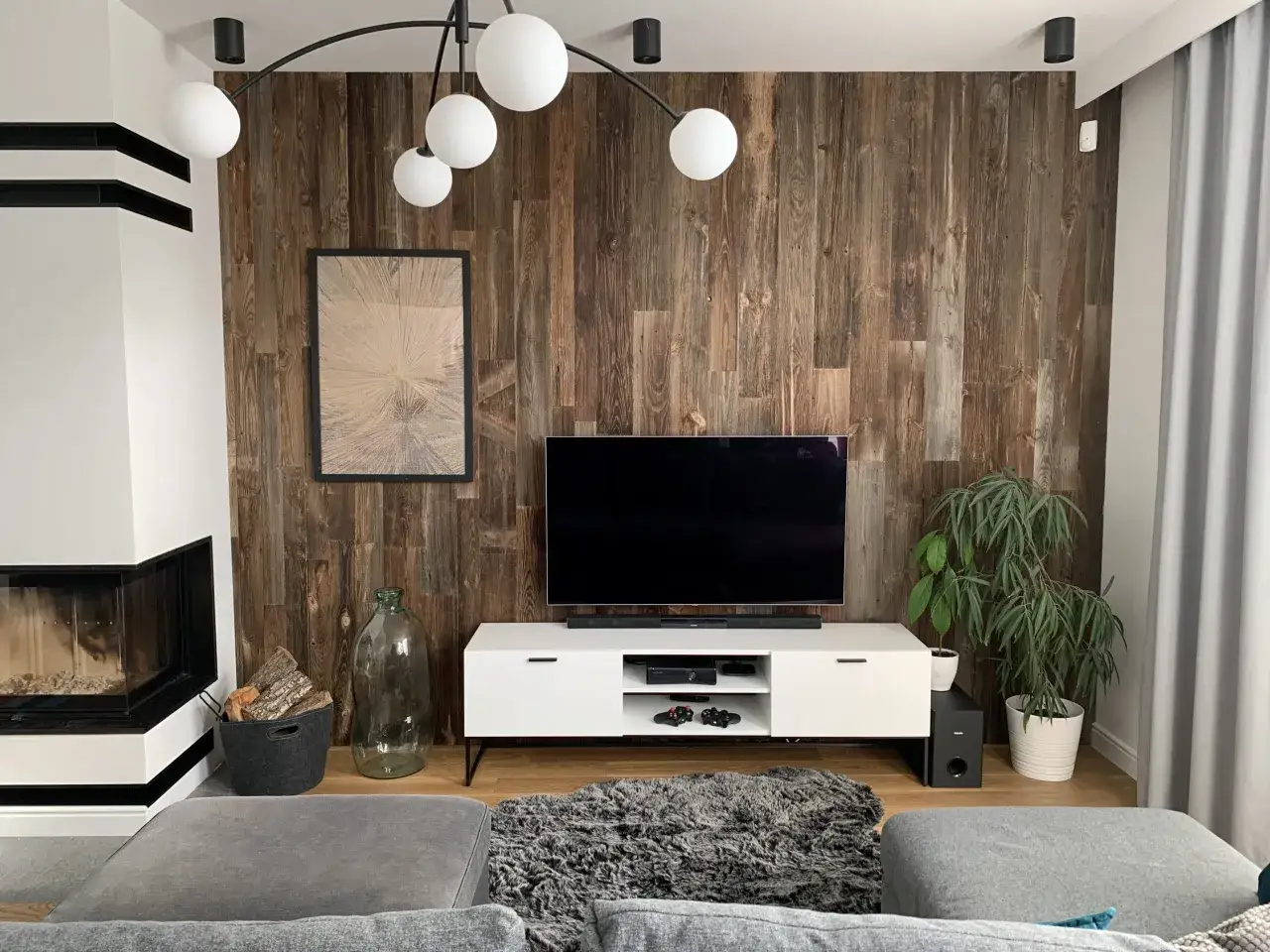 Nowoczesny salon z kominkiem i telewizorem na tle ściany z desek. Tapeta stare deski nadaje wnętrzu rustykalny charakter.