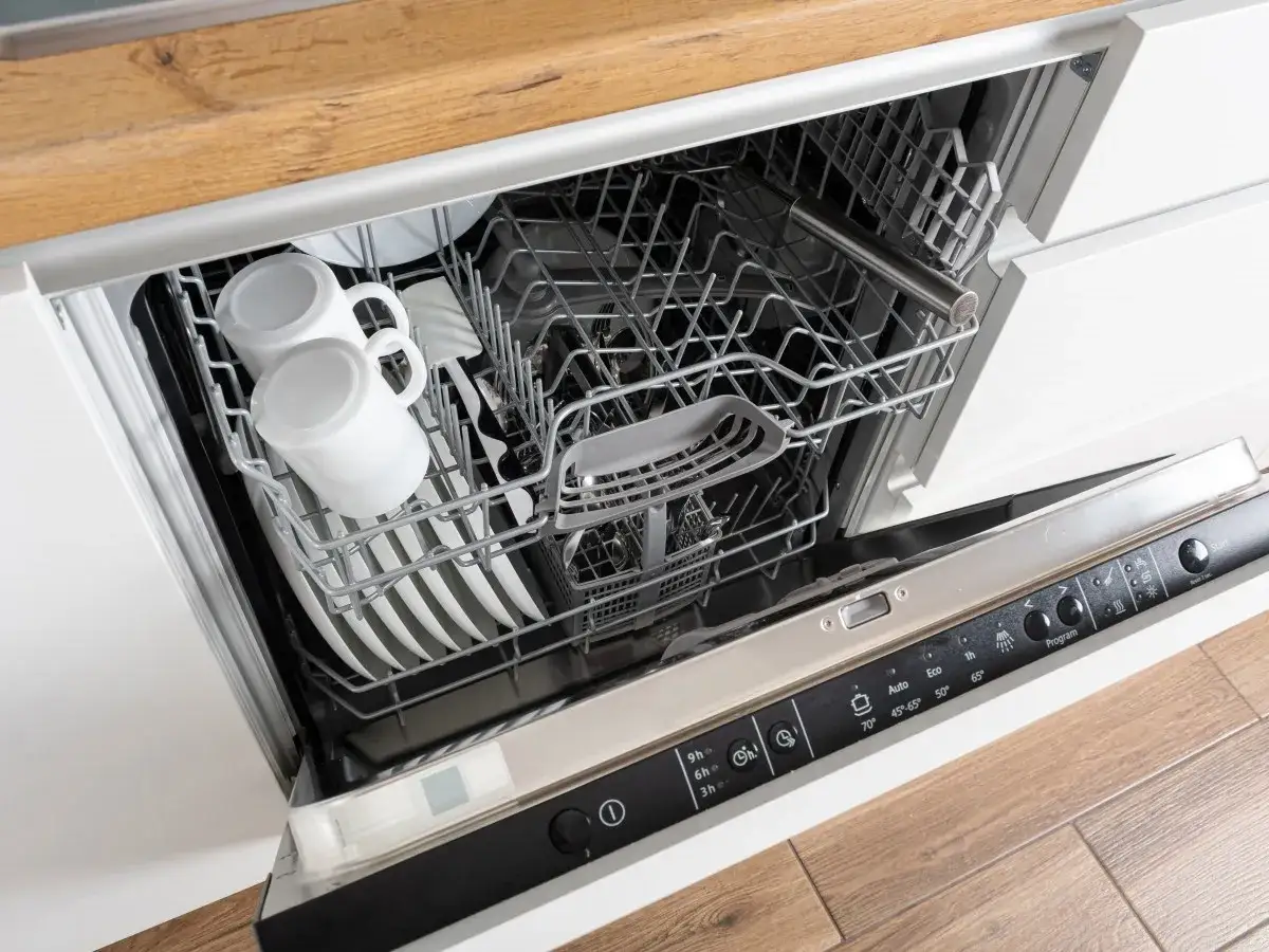 Wnętrze zmywarki Whirlpool 6th Sense z koszami pełnymi naczyń, w tym kubków i talerzy.
