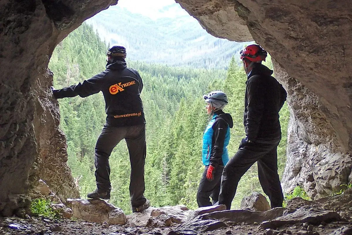 Trzech grotołazów w kaskach podziwia widok na Dolinę Kościeliską z wnętrza jaskini Mylnej.