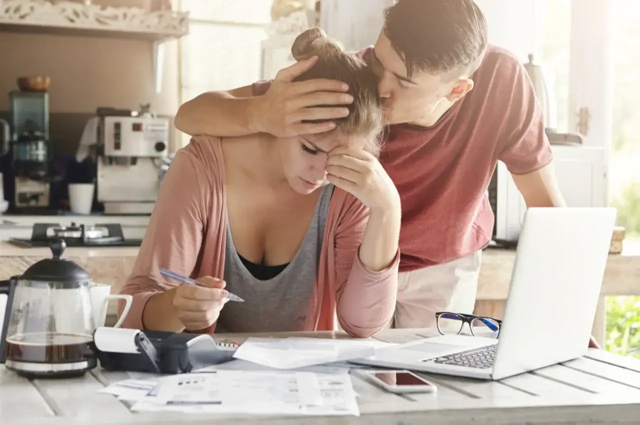 Mężczyzna pociesza kobietę przy biurku z dokumentami i laptopem.