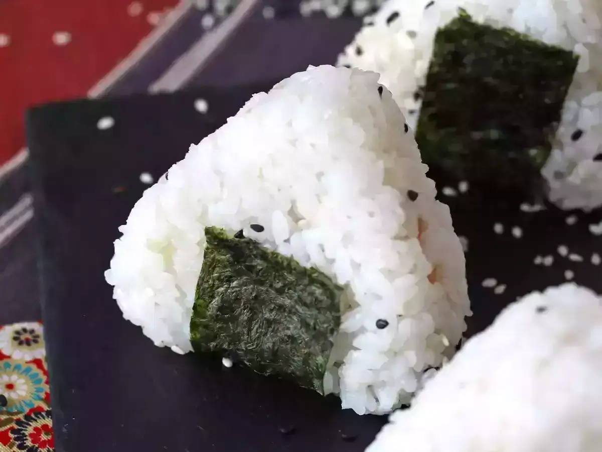 Trójkątne onigiri z tuńczykiem, ryżem i wodorostami nori, posypane sezamem.