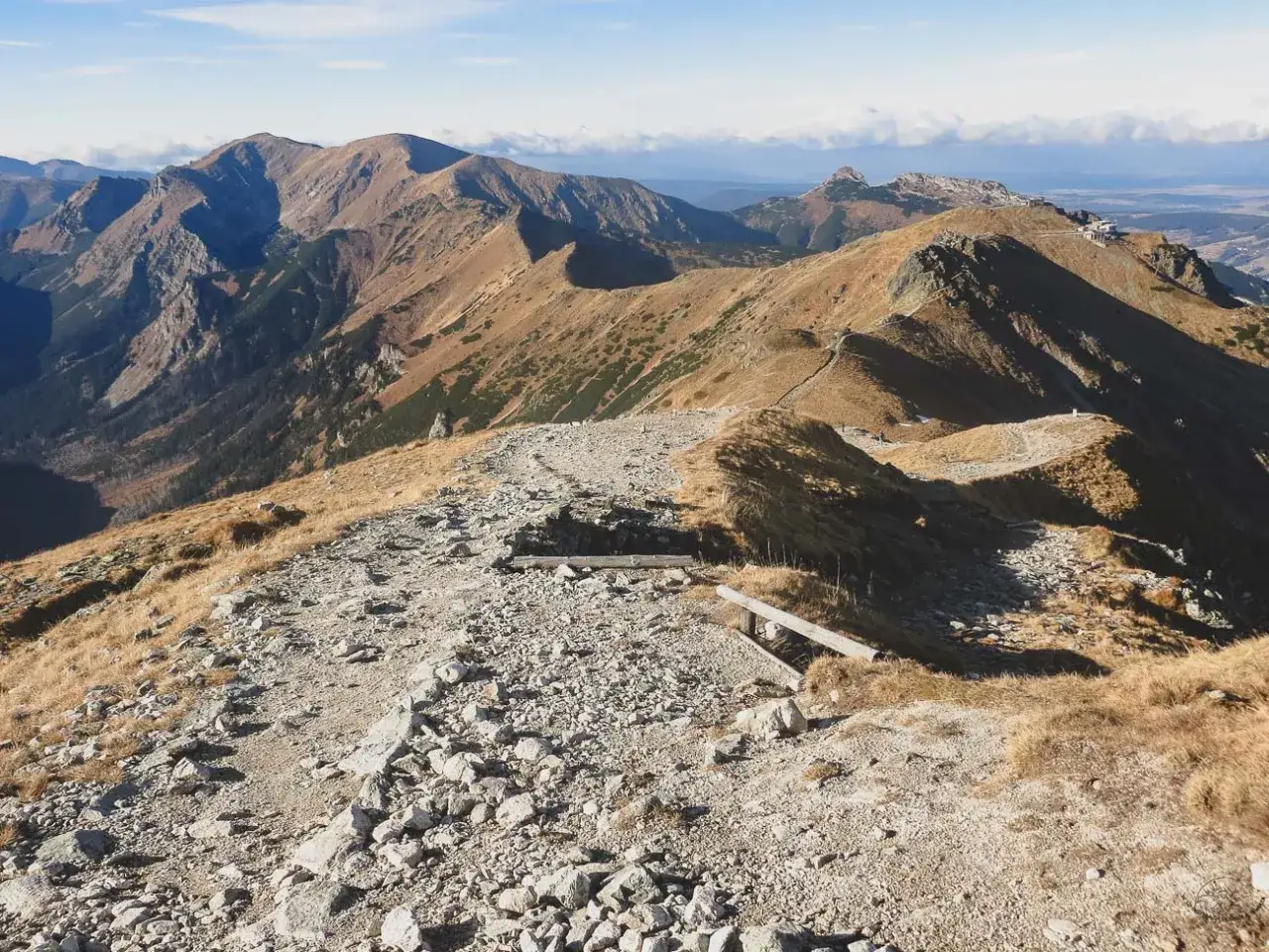 Kamienista ścieżka prowadzi przez trawiaste zbocza, ukazując najpiękniejsze doliny Zakopane. W oddali majaczą góry.