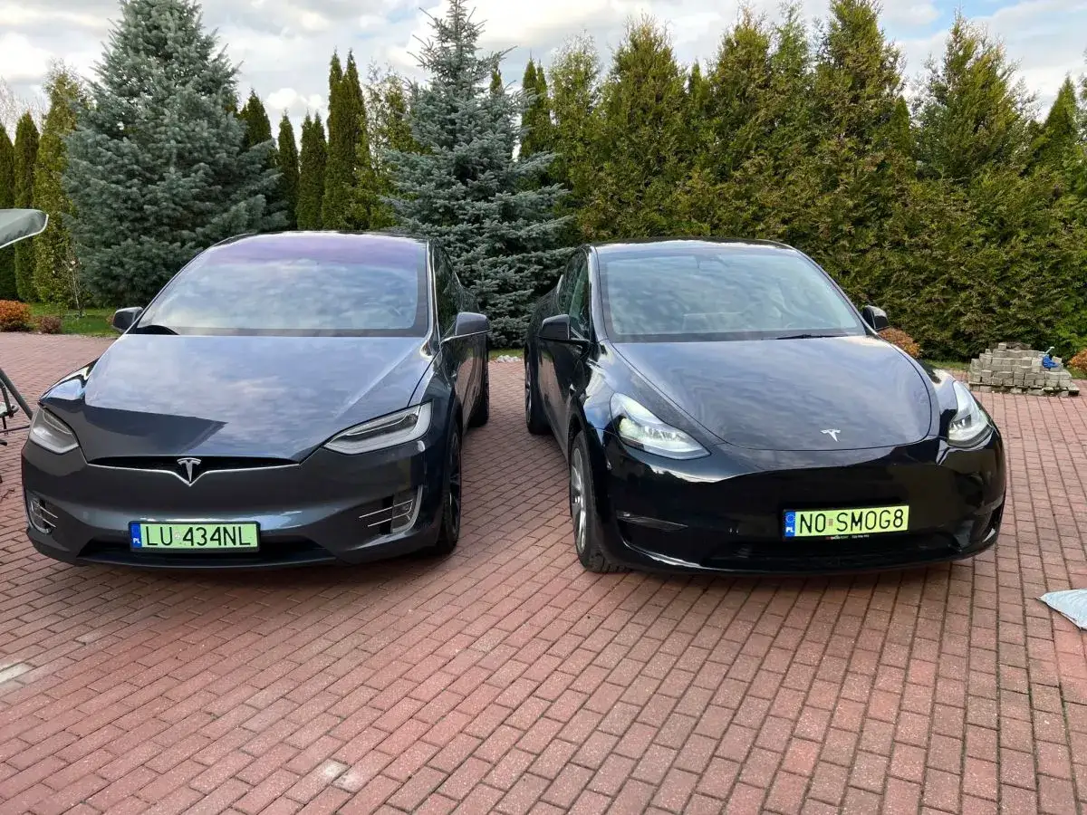 Dwa samochody Tesla, jeden ciemnoszary Model X, drugi czarny Model Y, stoją na podjeździe.