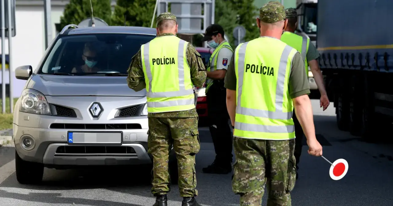 Policjanci w kamizelkach odblaskowych kierują ruchem podczas przejazdu przez Słowację. Kierowca w masce zatrzymuje się do kontroli.
