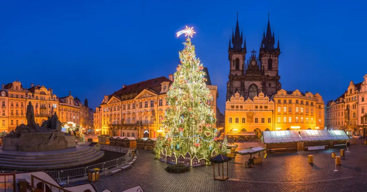 Jarmark bożonarodzeniowy w Pradze. Ogromna, oświetlona choinka na Rynku Staromiejskim, w tle gotycka architektura i zabytkowe kamienice.