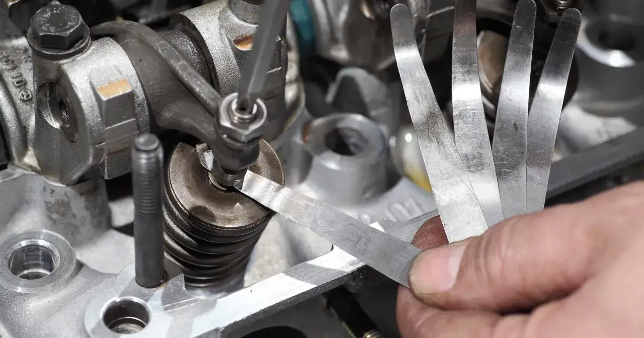 Dłoń z narzędziami do pomiaru szczelin zaworowych w silniku.