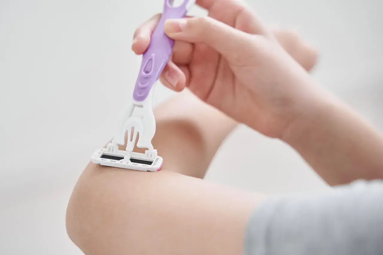 Dłoń trzymająca fioletowo-białą maszynkę do golenia goli skórę na ramieniu.