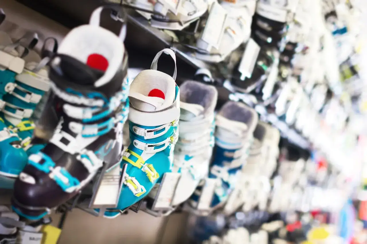 Rząd kolorowych butów narciarskich na półce sklepowej.