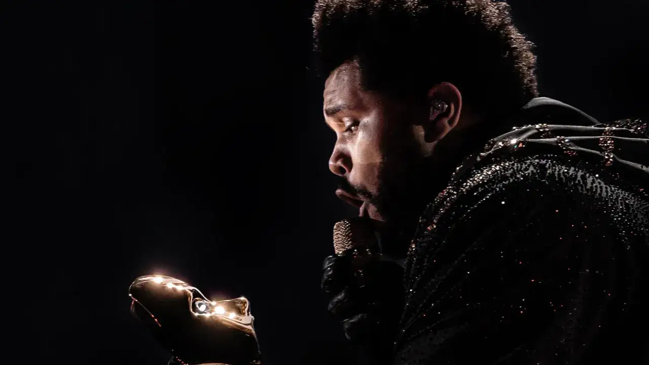 The Weeknd w błyszczącej kurtce, z mikrofonem w dłoni, zastanawia się, ile trwa koncert The Weeknd.