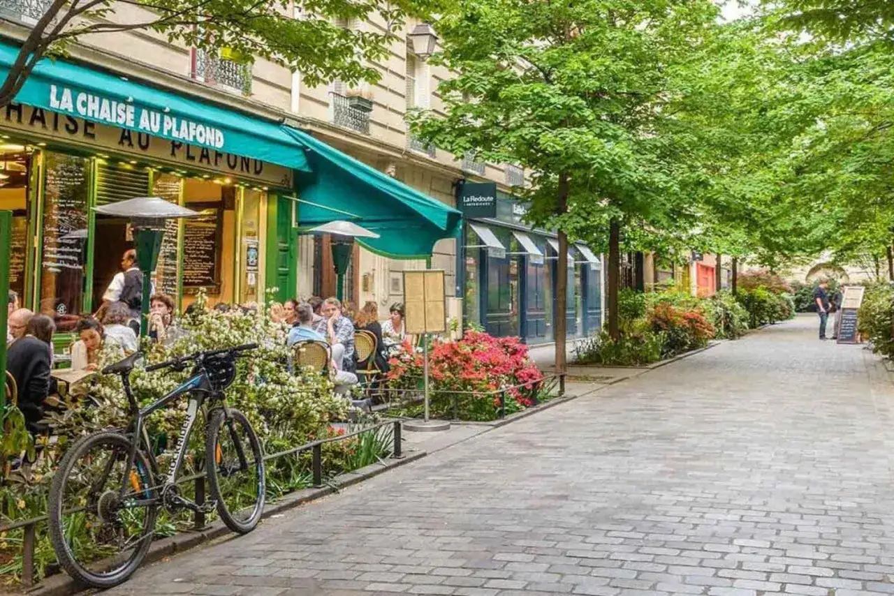 Urocza uliczka w paryskiej dzielnicy Le Marais. Ludzie siedzą przy stolikach kawiarni, a obok stoi rower.