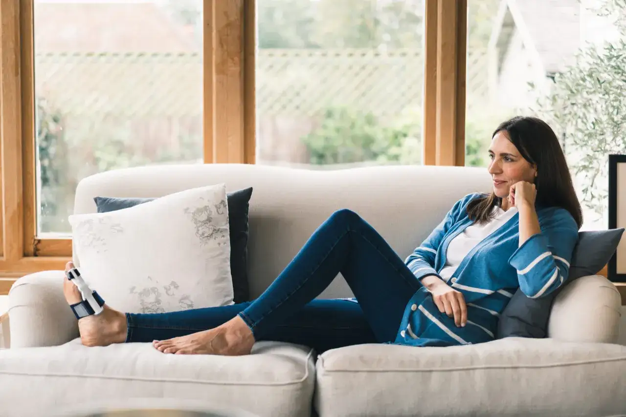 Kobieta odpoczywa na kanapie z aparatem na haluksy na stopie, zastanawiając się, czy aparaty na haluksy są skuteczne.