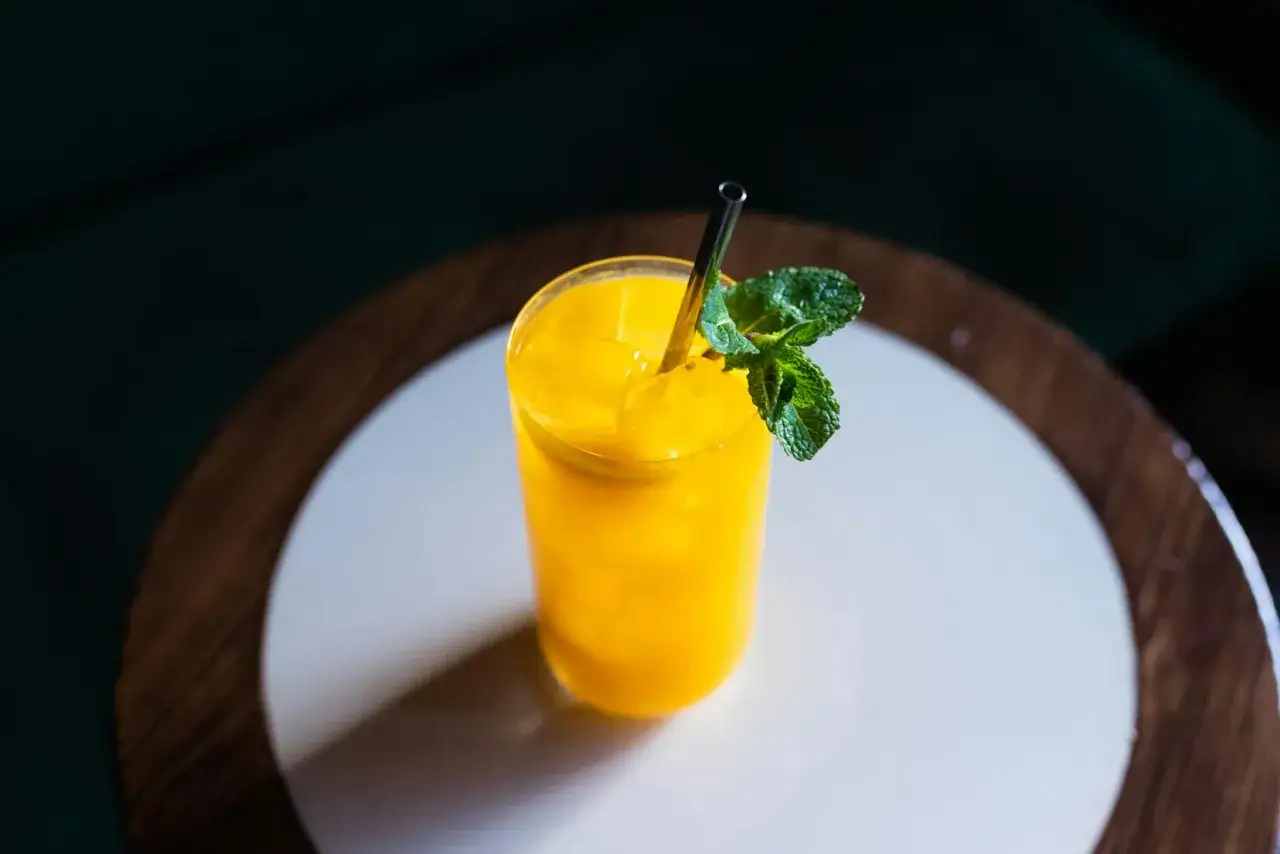 Orzeźwiający drink z mango, z kostkami lodu i listkiem mięty, podany w szklance ze słomką.