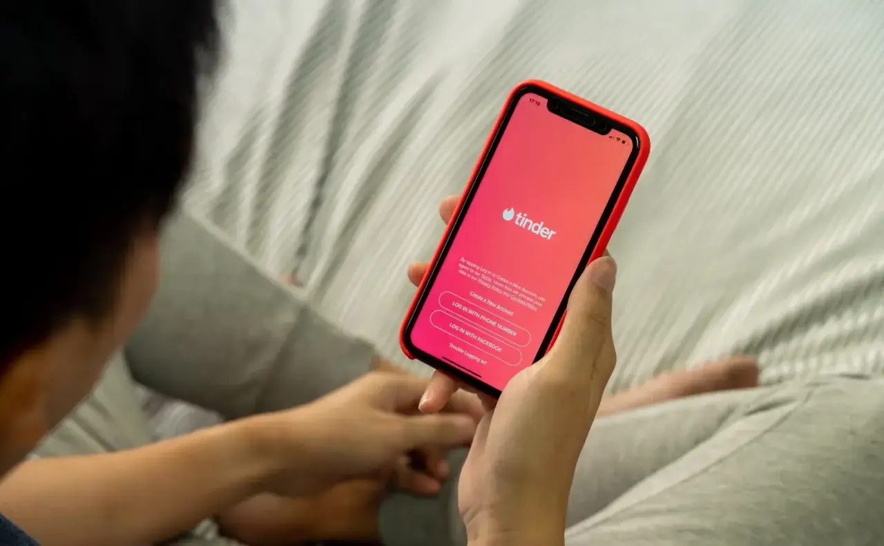Osoba trzyma telefon z aplikacją Tinder. Zastanawiasz się, czy warto założyć Tindera? Może to początek nowej znajomości.