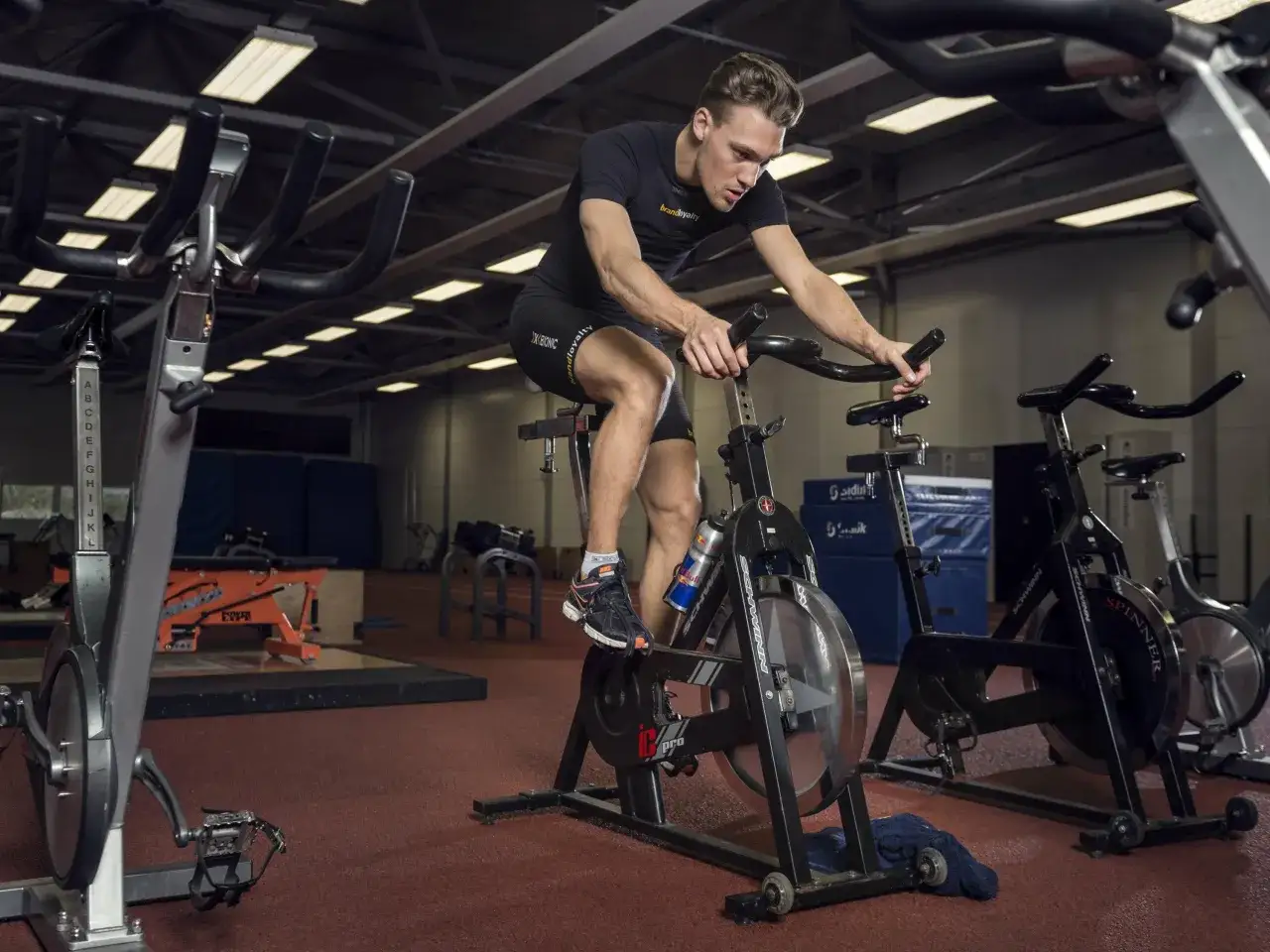 Mężczyzna na rowerze stacjonarnym, skupiony na treningu. Drobny interwał, pot spływa po jego skroniach.