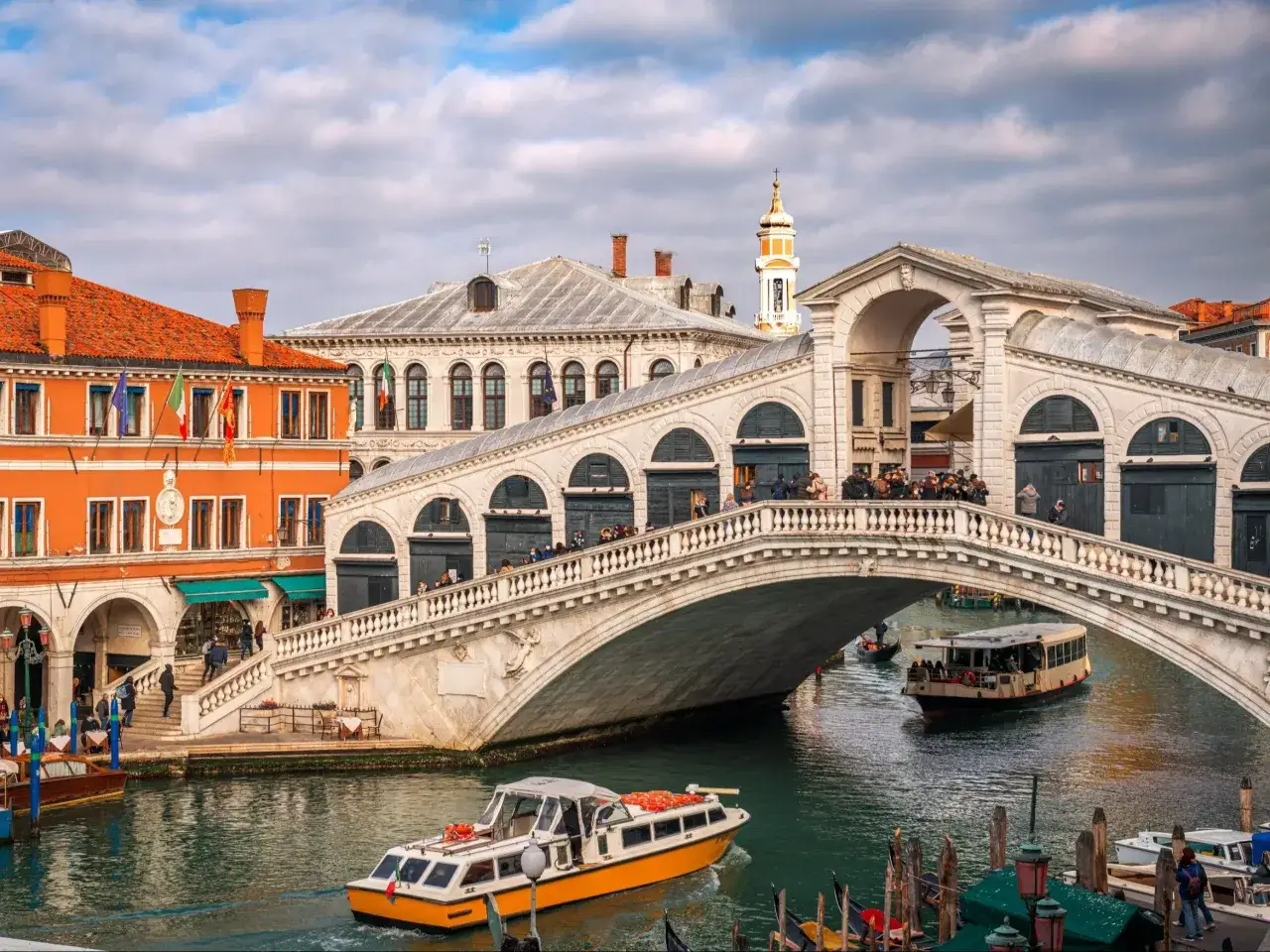Most Rialto Bridge w Wenecji, z łodziami na kanale i turystami na moście. Czy Wenecja jest bezpieczna? Tak, wygląda na to, że turyści czują się tu swobodnie.