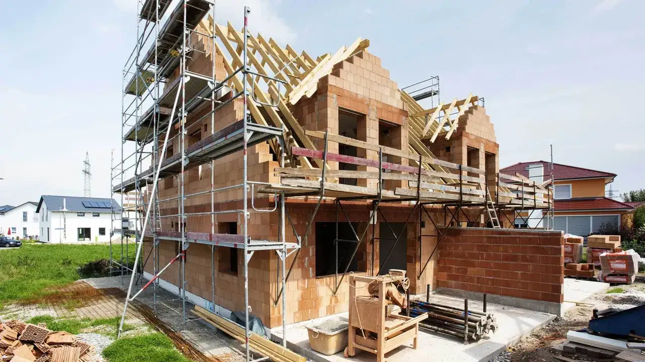 Budowa domu w toku: rusztowania, cegły, drewniane elementy dachu. To wszystko jest potrzebne do pozwolenia na budowę domu.