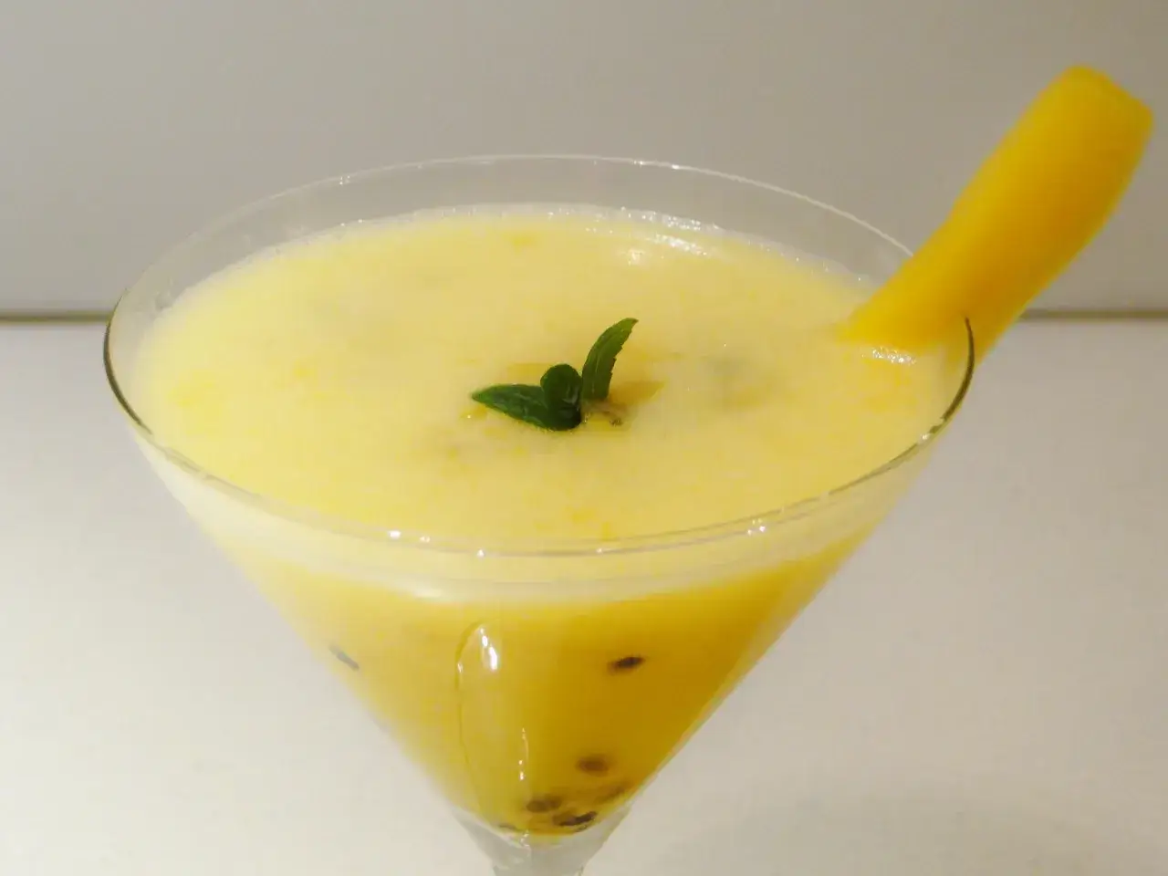 Orzeźwiający drink z marakują, ozdobiony listkiem mięty i kawałkiem mango.