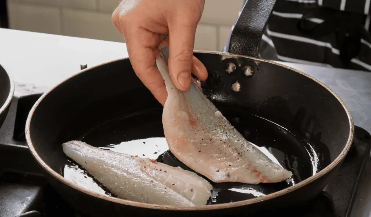 Ręka kładzie rybę na patelni z rozgrzanym olejem. Dowiedz się, na jakim tłuszczu smażyć ryby, by były idealne.