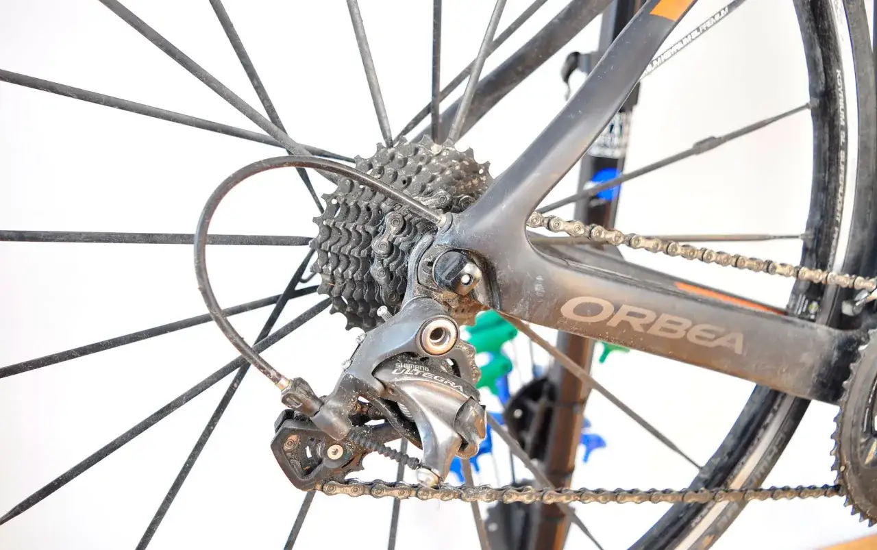 Tylna przerzutka Shimano Ultegra, kluczowy element przekładni rowerowej, na tle koła i ramy Orbea.