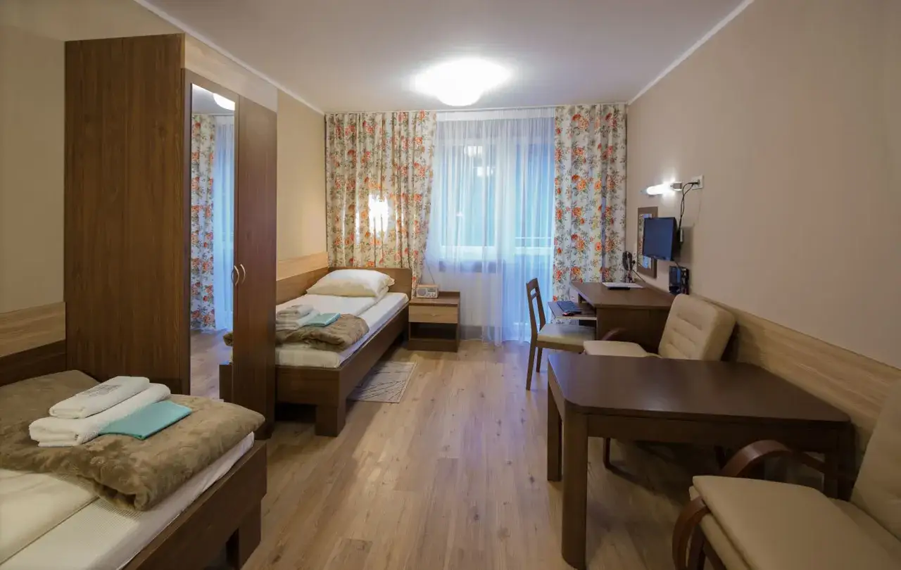 Pokój w sanatorium Włókniarz Busko-Zdrój: dwa łóżka, szafa, biurko z komputerem i stolik.