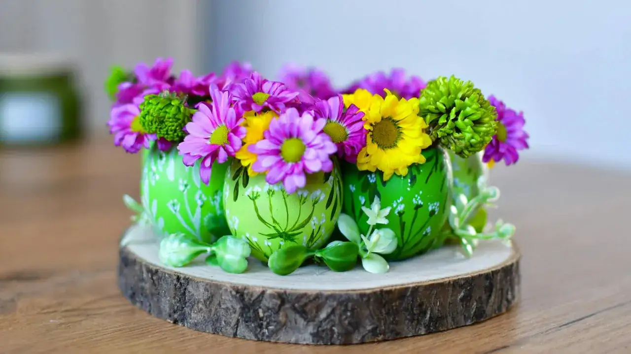 Nowoczesne, ręcznie robione stroiki wielkanocne z kwiatów w zielonych jajkach na drewnianym plastrze.