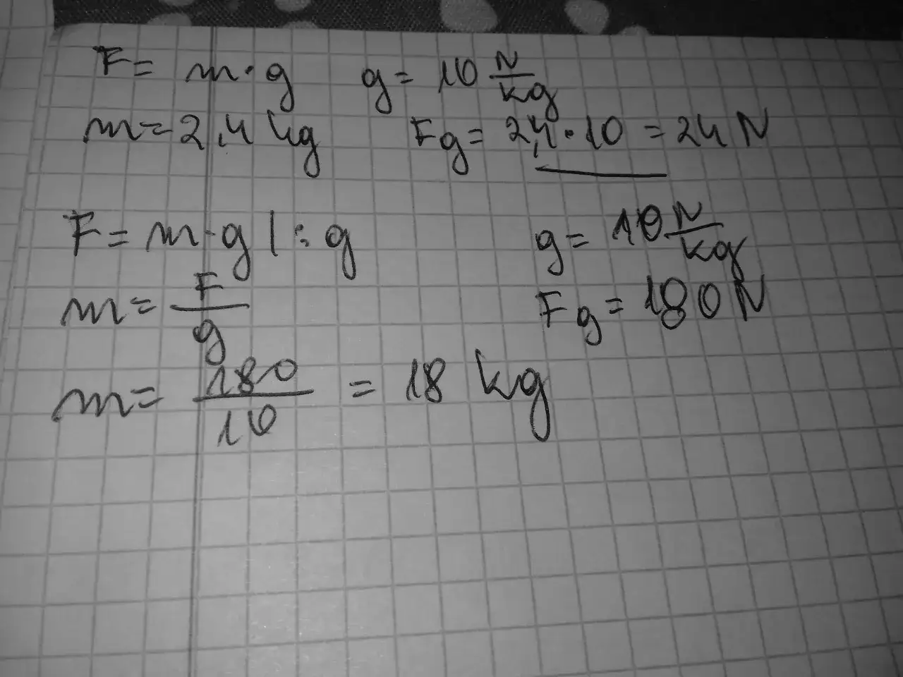 Ręcznie pisane wzory fizyczne na kratkowanym papierze, w tym F=m*g i obliczenia.