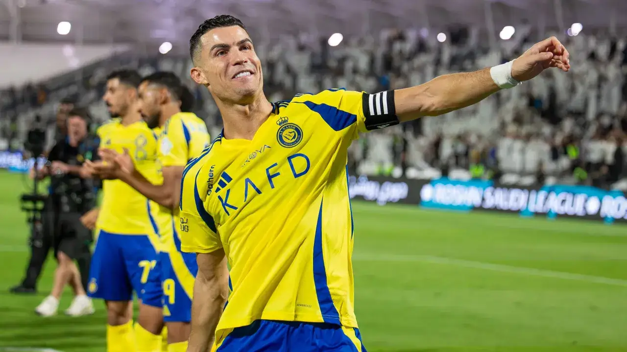 Uśmiechnięty Cristiano Ronaldo w żółtej koszulce Al Nassr, świętujący sukces. Jego zarobki w Arabii Saudyjskiej budzą podziw.