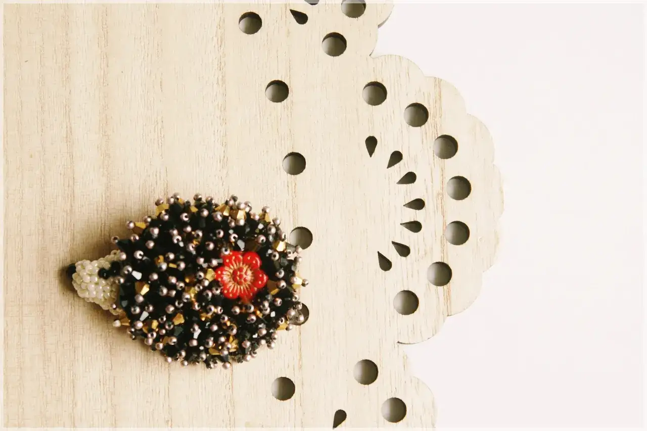 Uroczy jeżyk z koralików, ozdobiony czerwoną kwiatuszką. Piękne wyszywanie koralikami wzory.