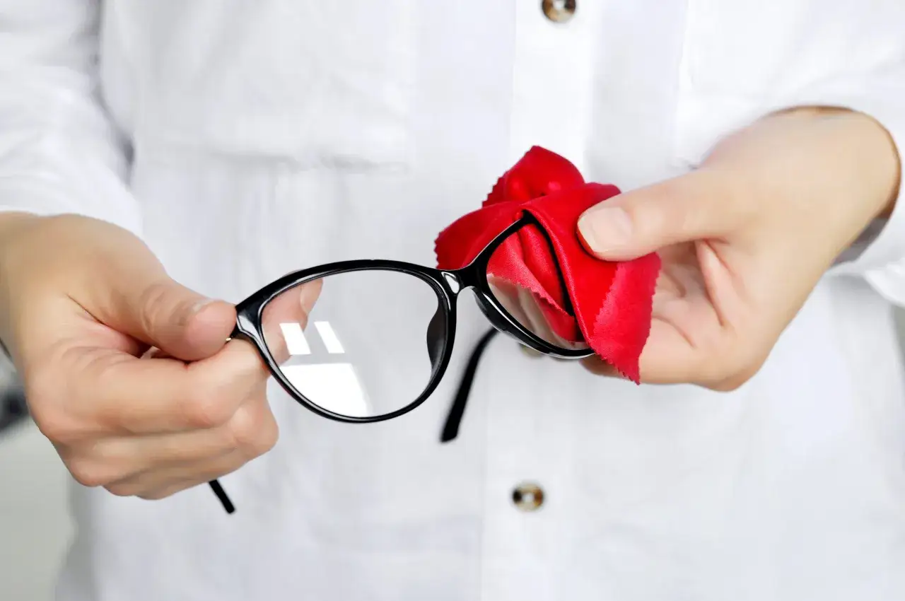 Dłonie czyszczą czarne okulary czerwoną ściereczką z mikrofibry. Dowiedz się, czym czyścić okulary, by były idealnie przejrzyste.