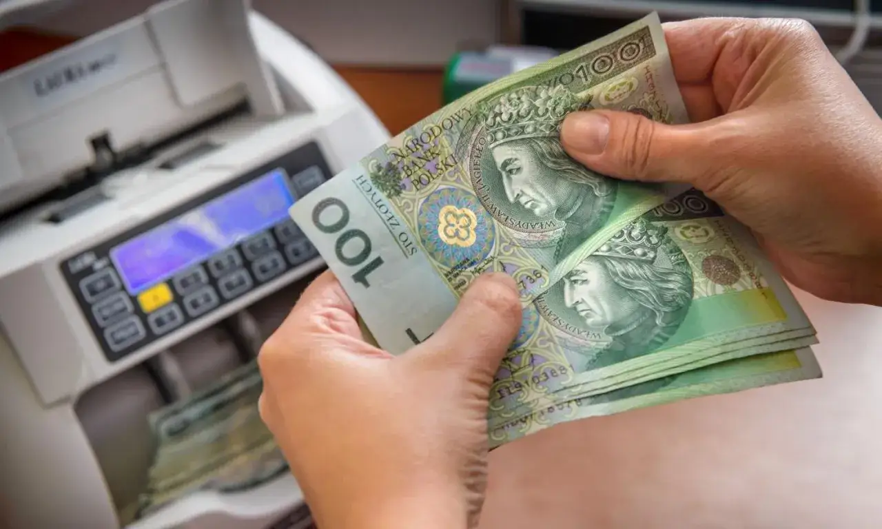 Ręce trzymają banknoty 100 zł obok licznika pieniędzy. Czy przy wcześniejszej spłacie kredytu należy się zwrot odsetek?