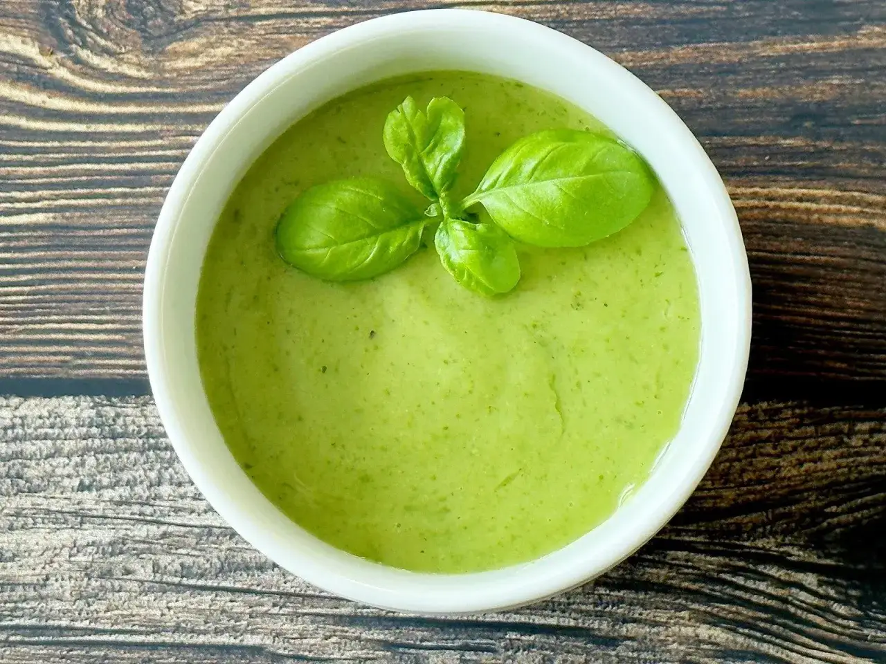 Zielony sos winegret w białej miseczce, ozdobiony listkami bazylii, na drewnianym tle.