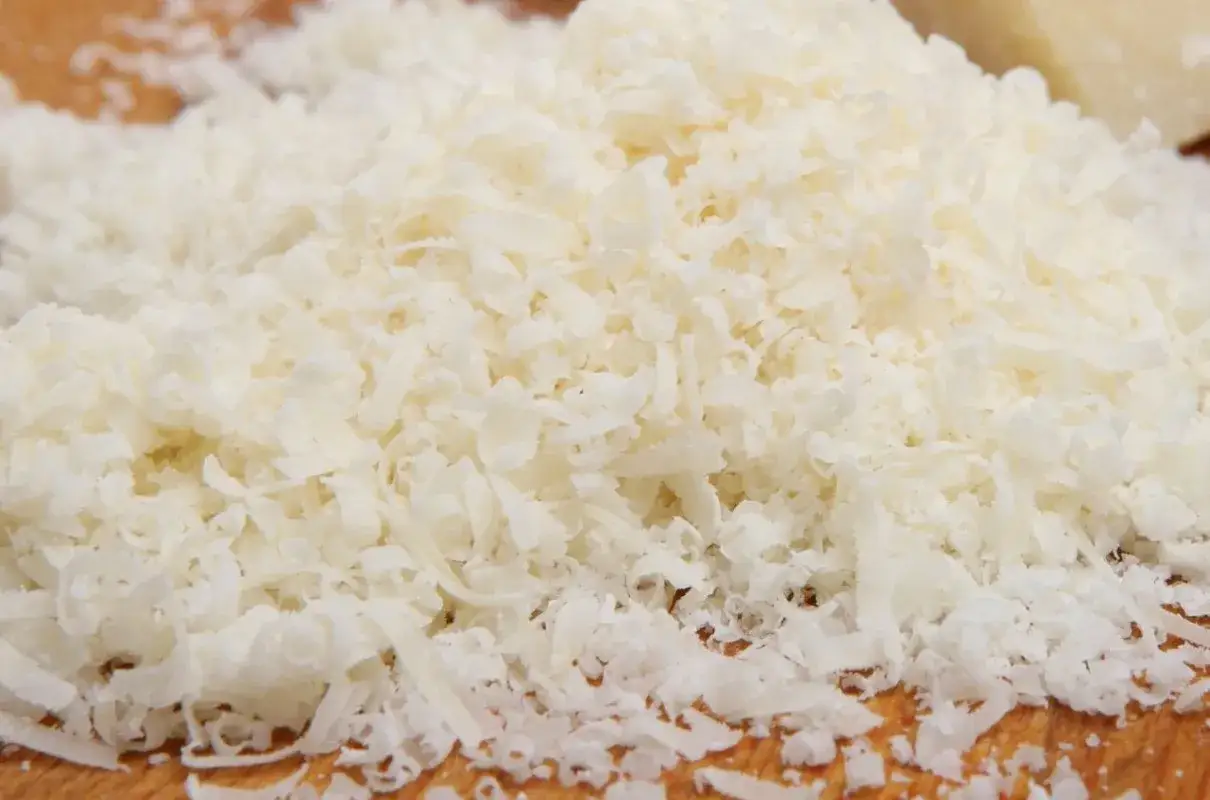 Stos tartych kawałków parmezanu na drewnianej desce.