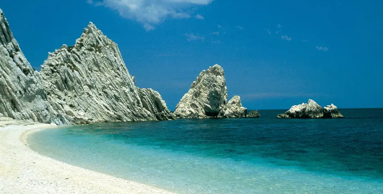 White pebble beach with turquoise water and dramatic white rock formations under a clear blue sky.