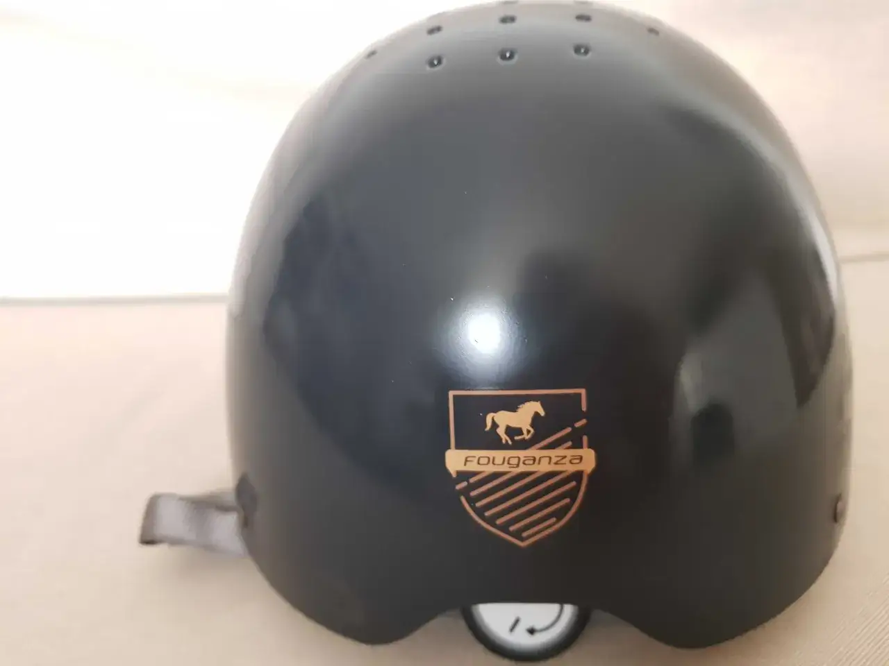 Czarny kask jeździecki Fouganza z logo konia i tarczą.