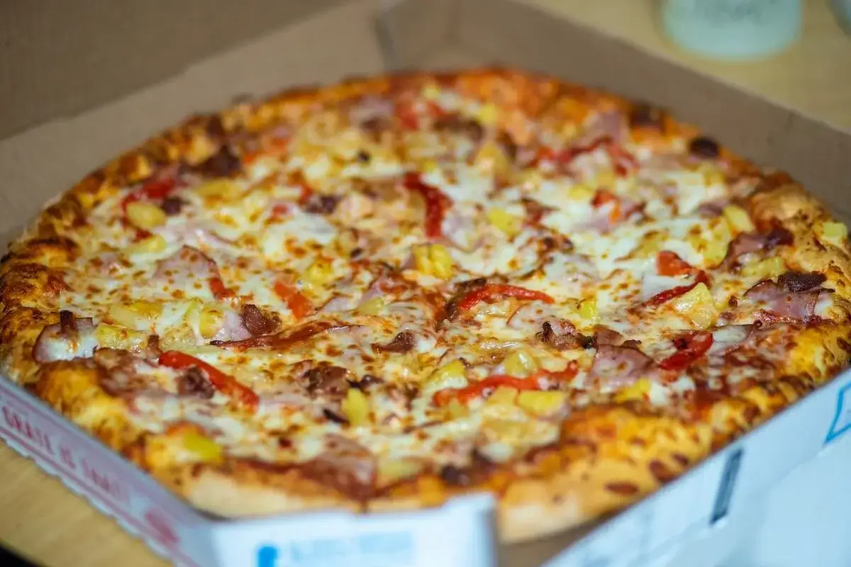 Pyszna, gorąca mrożona pizza w mikrofali, prosto z pudełka. Złocisty ser, kawałki ananasa i papryki kuszą apetycznie.