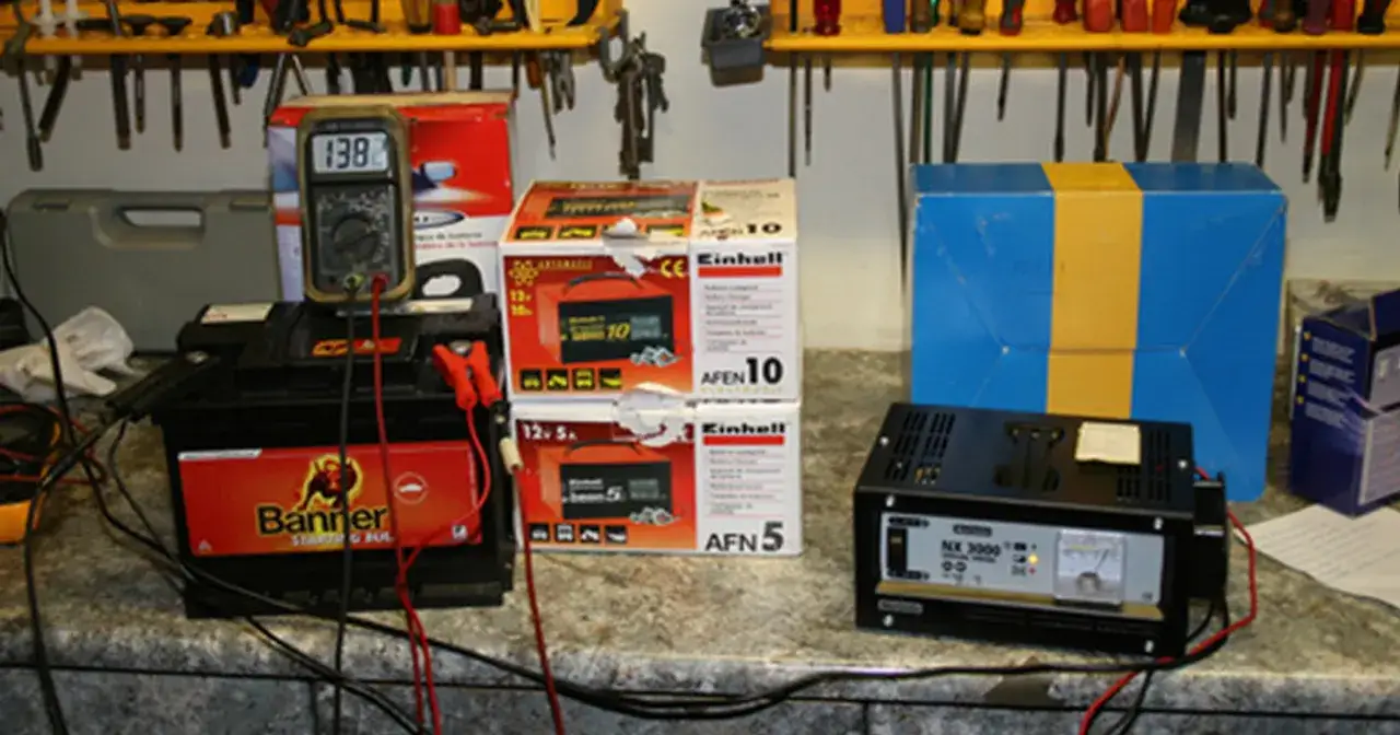 Prostownik samochodowy podłączony do akumulatora, obok pudełka z prostownikami.