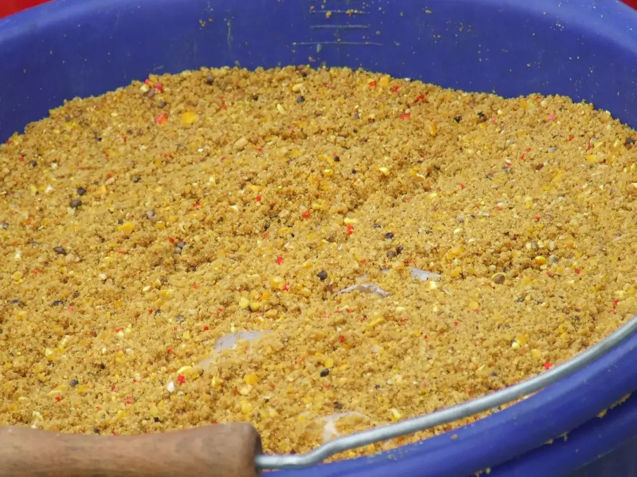 Zbliżenie na wiadro z zanętą wędkarską, widoczne ziarna kukurydzy i inne składniki.