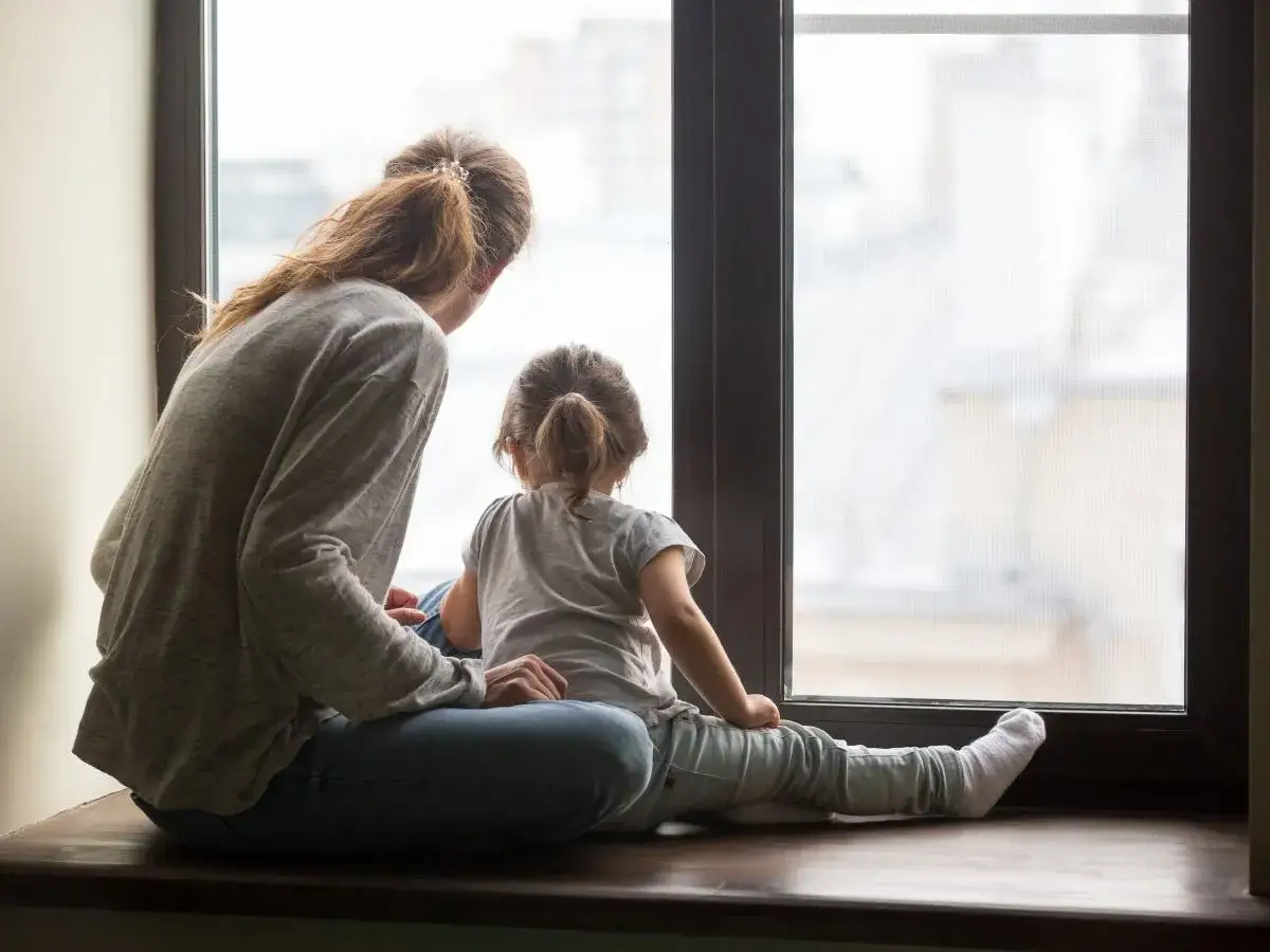 Kobieta z dzieckiem siedzą na parapecie i patrzą przez okno.
