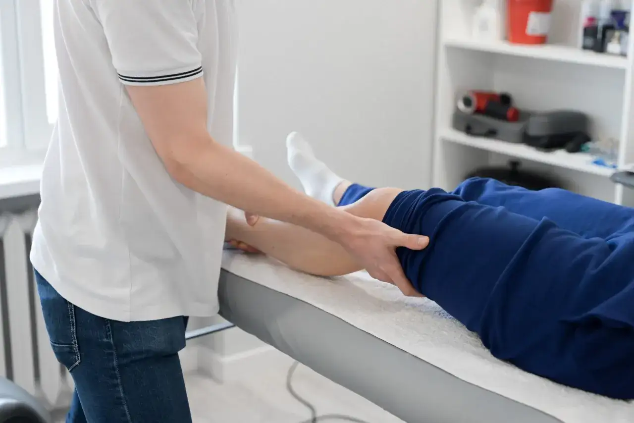 Fizjoterapeuta wykonuje masaż nogi pacjenta leżącego na kozetce.