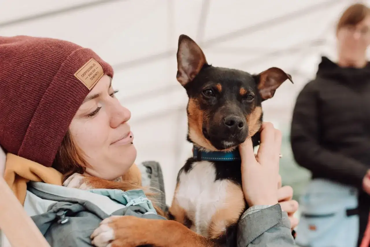 Uśmiechnięta wolontariuszka tuli małego psa. Dowiedz się, jak zostać wolontariuszem w schronisku i pomagać zwierzętom.