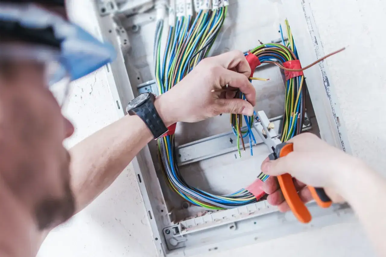 Elektryk pracuje nad prostą instalacją elektryczną, przycinając kolorowe przewody w skrzynce rozdzielczej.