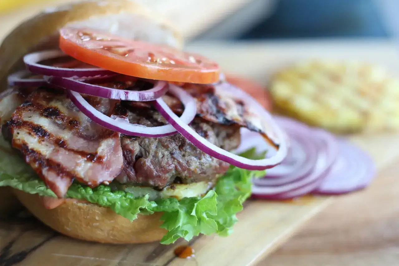 Soczysty burger z bekonem, pomidorem i czerwoną cebulą na desce.