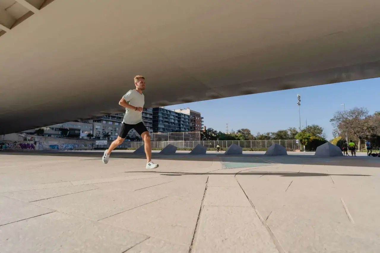 Mężczyzna w lekkim stroju sportowym biegnie po betonowym placu, przygotowując się do biegu na 10 km. W tle budynki i drzewa.