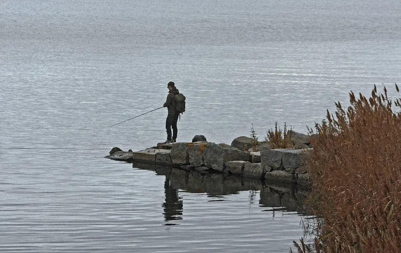 Mężczyzna z plecakiem łowi ryby z kamienistego brzegu.