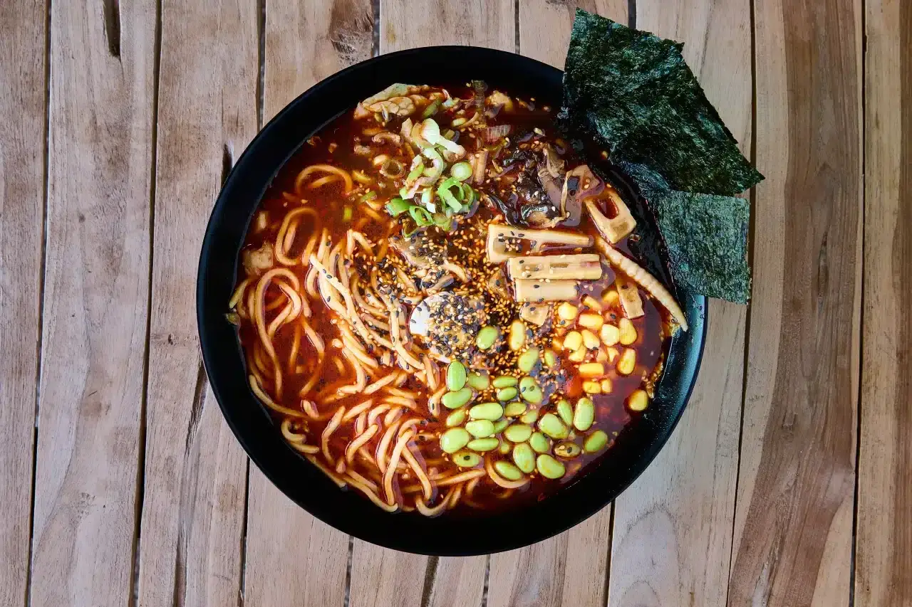 Miseczka aromatycznych dań z makaronem ramen, pełna edamame, kukurydzy, grzybów i nori, na drewnianym tle.