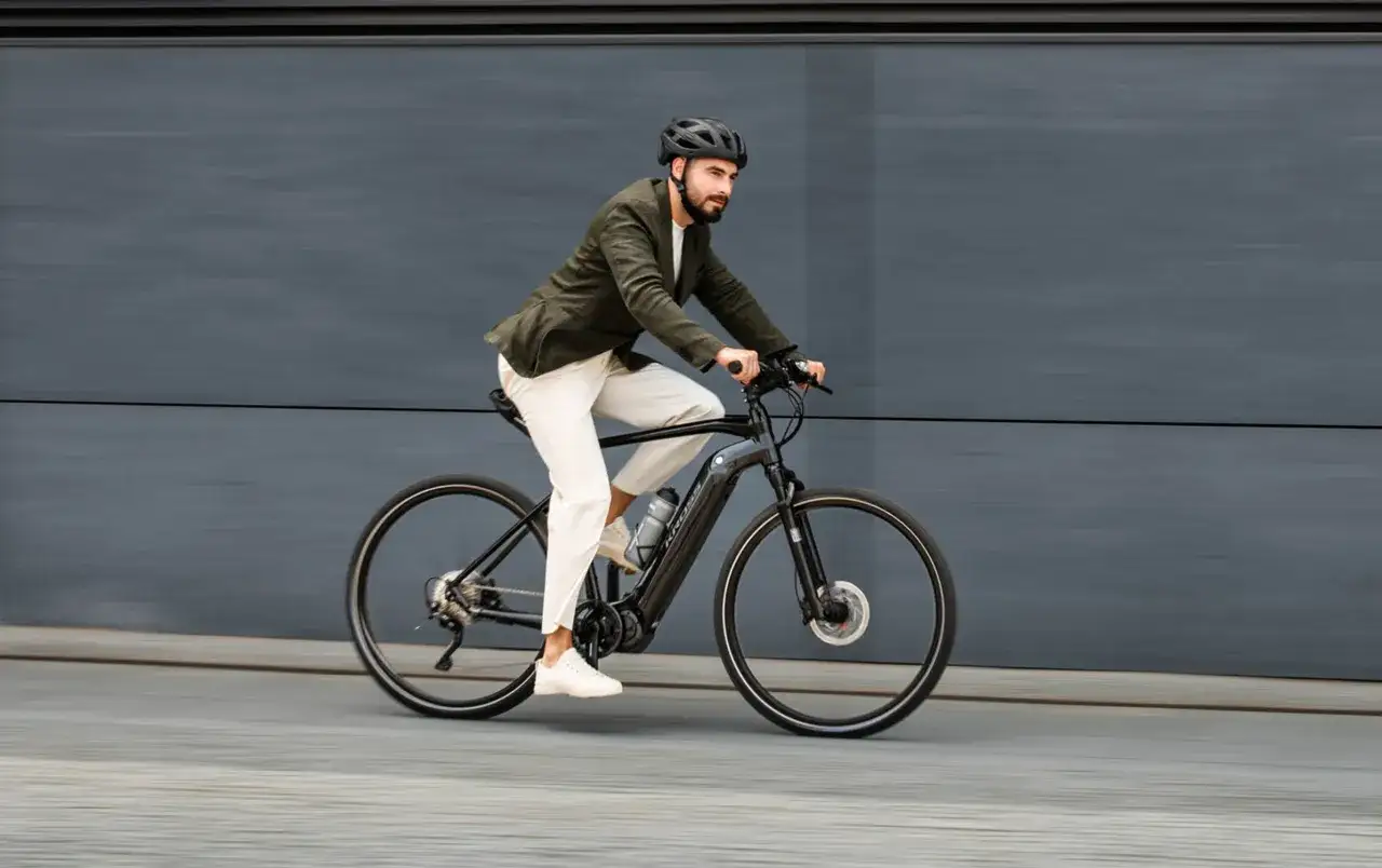 Mężczyzna w kasku i marynarce jedzie na rowerze elektrycznym po szarym tle.